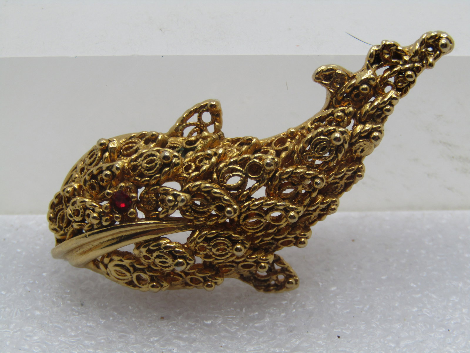 Vintage Filigree Fish/Whale Brooch, Rhinestone Eye, 1960's-1970's: Vintage Filigree Fish/Whale Brooch, Rhinestone Eye, 1960's-1970's. It looks whale like with red rhinestone eye and a smooth gold tone large mouth with fins. The bodly has open work fiigree raised desi