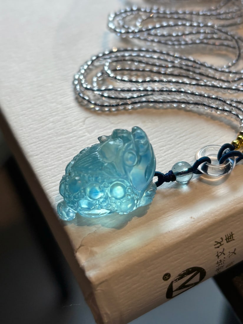 Natural Aquamarine Hand-Carved Fortune Toad Pendant with Certificate: Title: Natural Aquamarine Hand-Carved Fortune Toad Pendant with Certificate Origin: Chinese Date/Period: After2025 Materials: Aquamarine Dimensions: 26x18x16(mm) 1.02x0.71x0.63(inches) Weight 0.03
