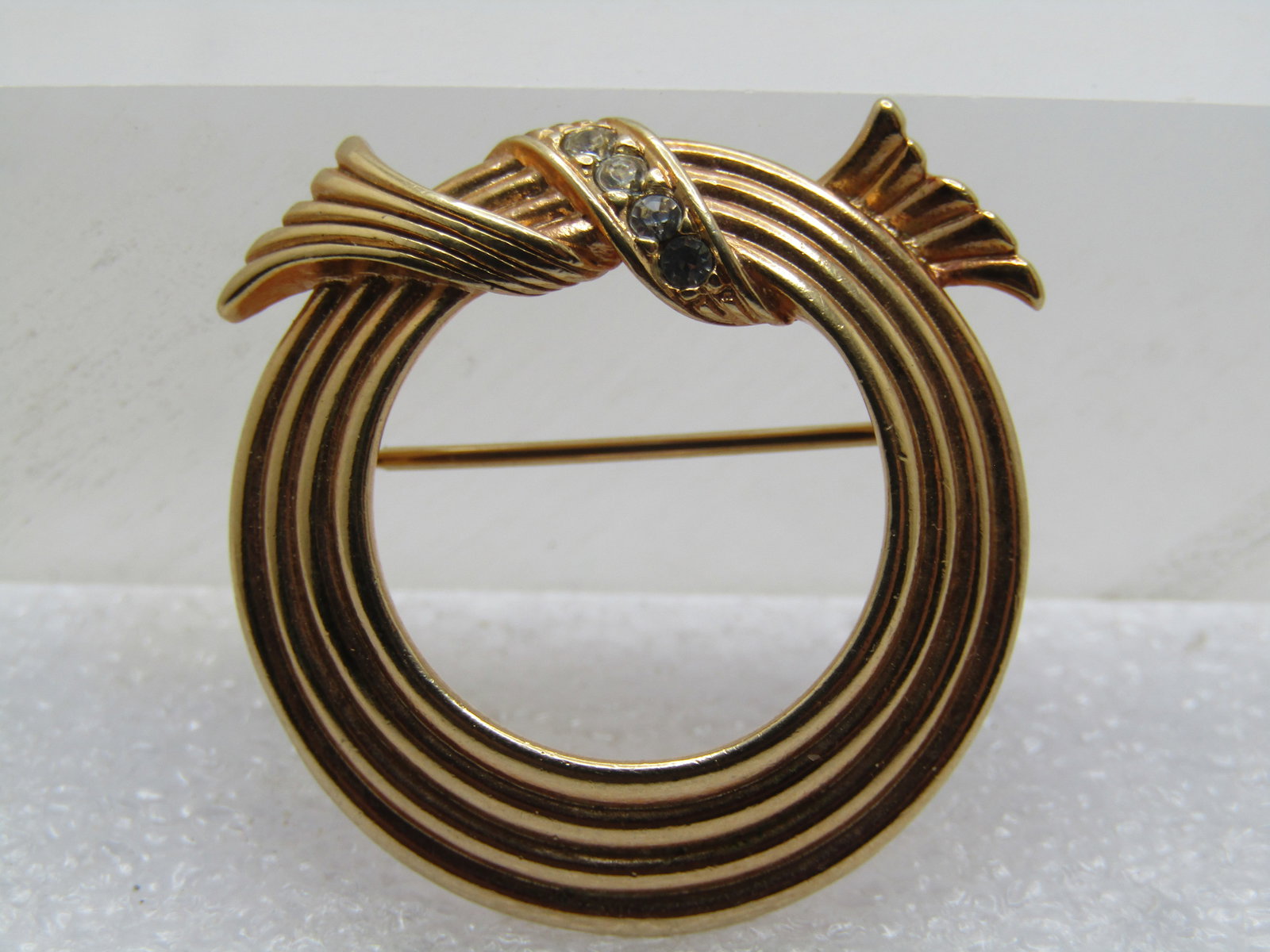 Vintage Circle Brooch with Rhinestone Looped Bow on Top, Signed Avon, 1970's: Vintage Circle Brooch with Rhinestone Looped Bow on Top, Signed Avon, 1970's. It has a tapered design with four fused cirles - angled toward the top with a looped bow around the top with rhinestone