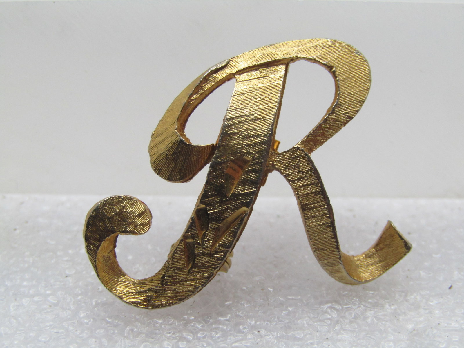 Vintage Initial R Brooch, Signed Mamselle, 1960's: Vintage Initial R Brooch, Signed Mamselle, 1960's. Gold tone with diamond cut notches cut into the script R. It is appx. 1.25" tall and wide. Very good condition. Locking clasp. (W31623.5 SS13730