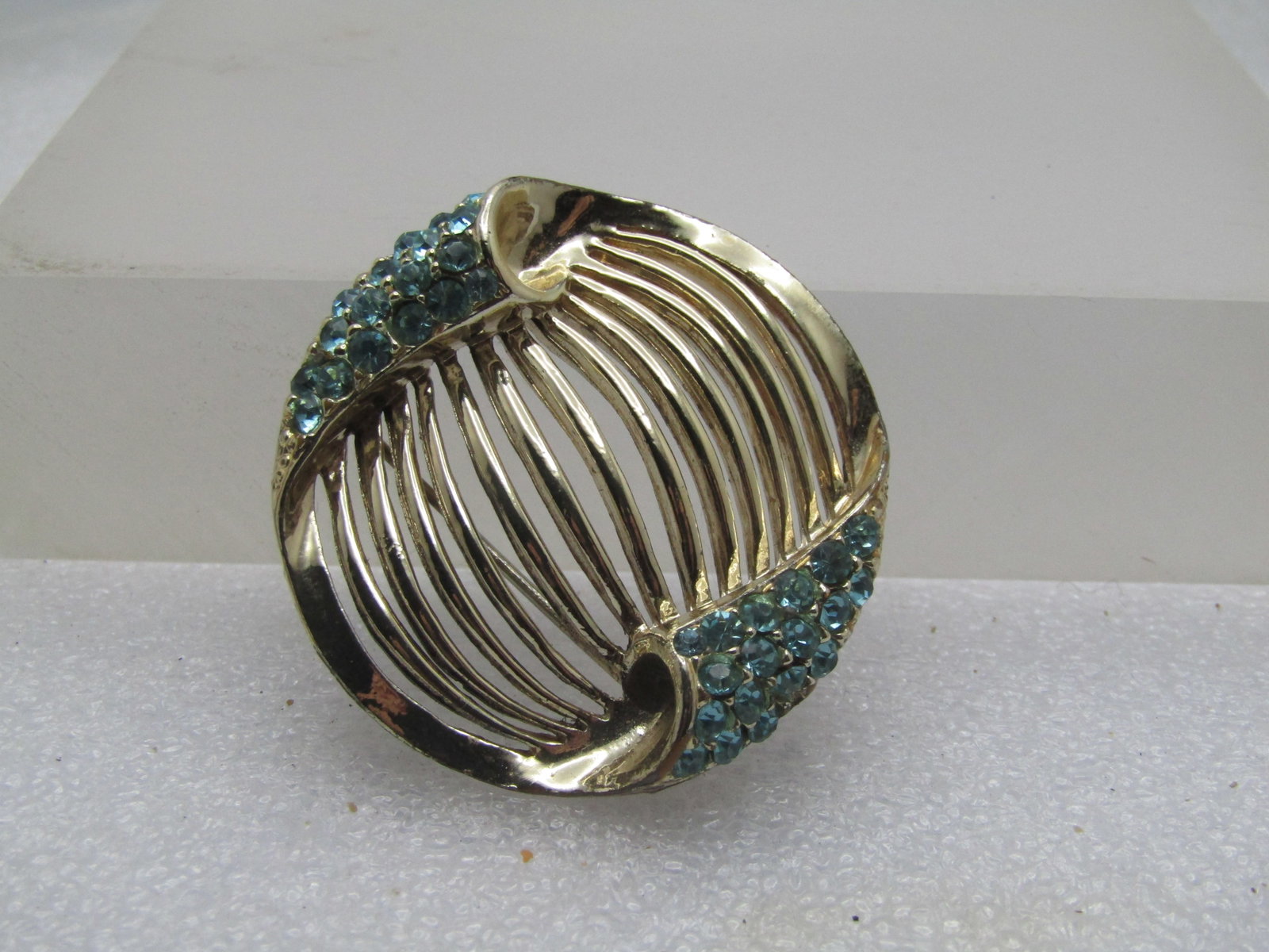 Vintage Aqua Rhinestone Brooch Open Ribbed, 1960's: Vintage Aqua Rhinestone Brooch Open Ribbed, 1960's. It is appx. 1.75" one directino and 1-5/8" the other. The center is made of domed ribs with open space between them - gold tone. The sides have a cu