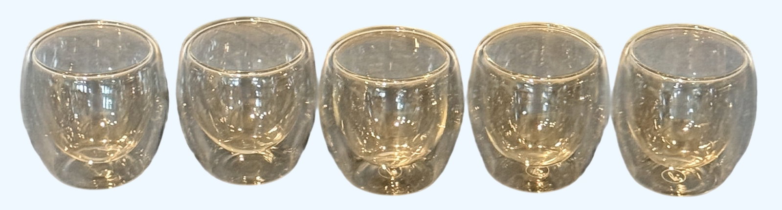 Set of Five Double-Walled Glass Tumblers: A contemporary set of five double-walled clear glass tumblers, designed for thermal insulation. Each tumbler features a sleek, modern aesthetic with a smooth, rounded form. The double-walled construct