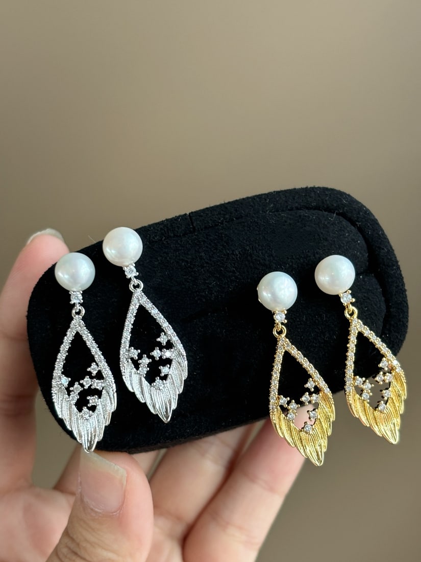 Natural Pearl Earrings: Title: Natural Pearl Earrings Description: These earrings feature natural pearls set in a wing-shaped design, showcasing a silky texture with rich gold and cool white hues. The gentle luster of the
