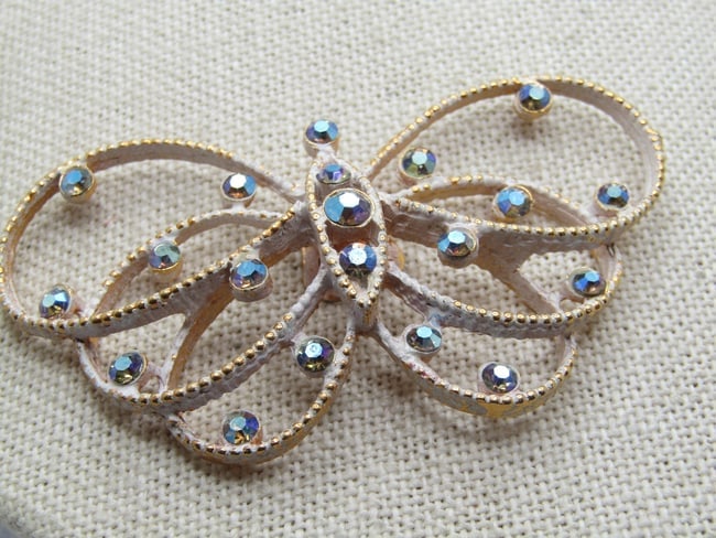 Vintage Rhinestone Butterfly Dress Clip, White Enameling, 1950's-1960's. It is appx. wide and 1.25": Vintage Rhinestone Butterfly Dress Clip, White Enameling, 1950's-1960's. It is appx. wide and 1.25" tall with dotted like gold tone frame washed in white enameling. The rhinetones are blue aurora bore