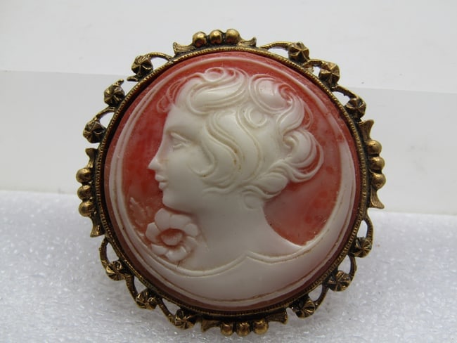 Vintage Round Cameo Brooch, 1960's, 1.75": Vintage Round Cameo Brooch, 1960's, 1.75". This has an ornate short frame with beaded and star scrolled accents. Gold tone, locking clasp with a brick colored background and white cameo lady with a fl