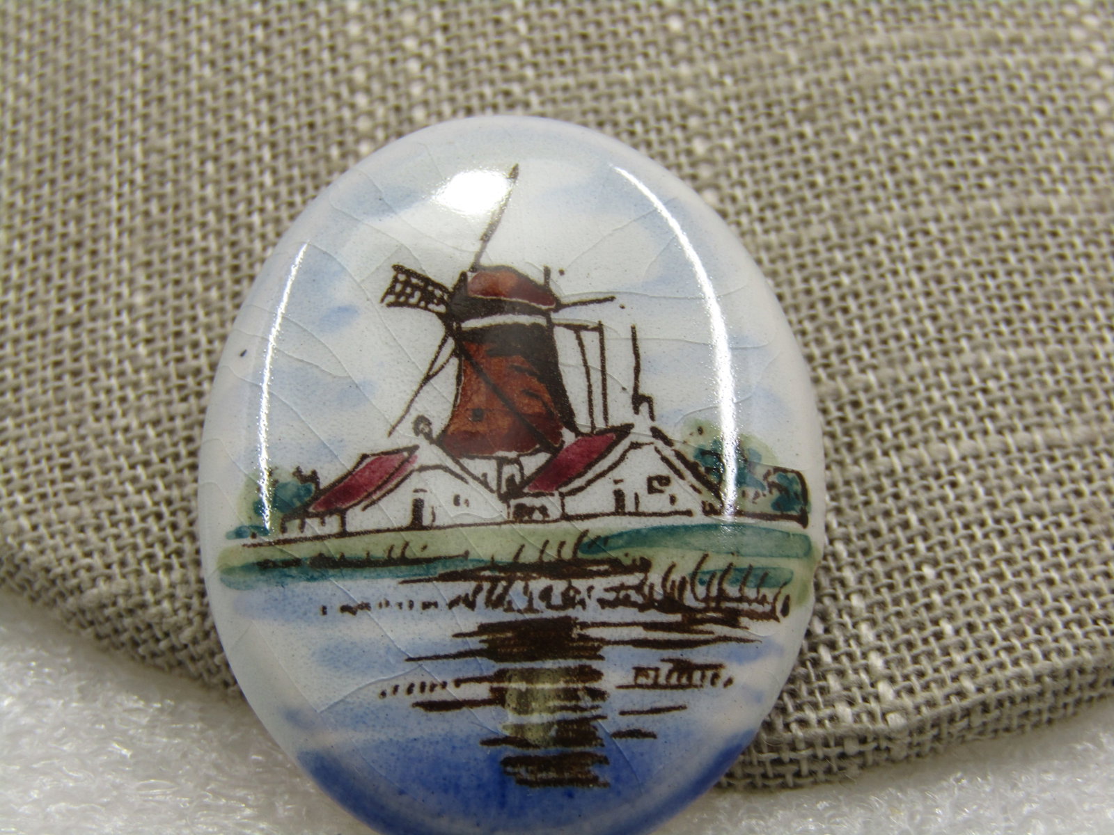 Vintage Painted Porcelain Windmill Brooch, 1.5": Vintage Painted Porcelain Windmill Brooch, 1.5" by 1.25. Possibly transfer image. Colors are shades of blue and green with a brown/red/white windmill and outer houses images. Age is mid-century. Good