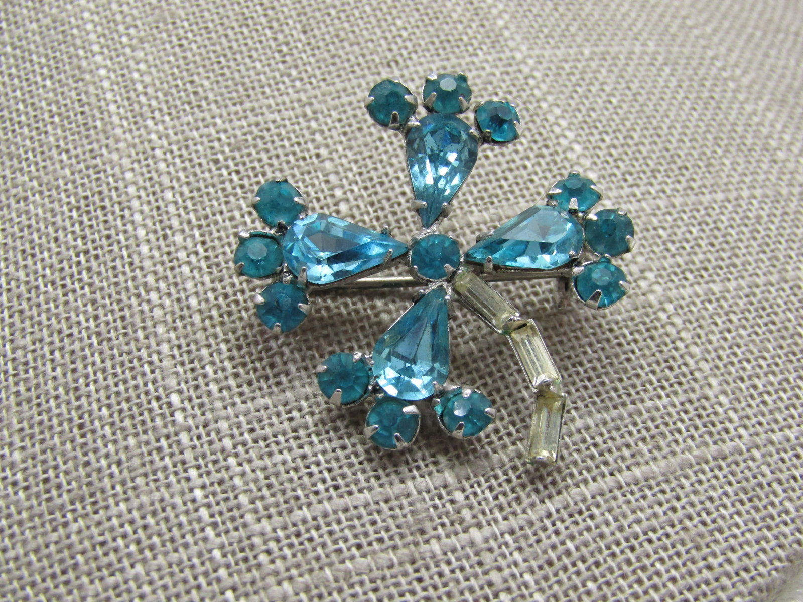 Vintage Aqua & Clear Rhinestone 4 Leaf Brooch, 1.75": Vintage Aqua & Clear Rhinestone 4 Leaf Brooch, 1.75". Thematic of four-leaf clover with four petals and a curved clear baguette stem. 1960's. Silver tone. Not signed by the maker. Very good
