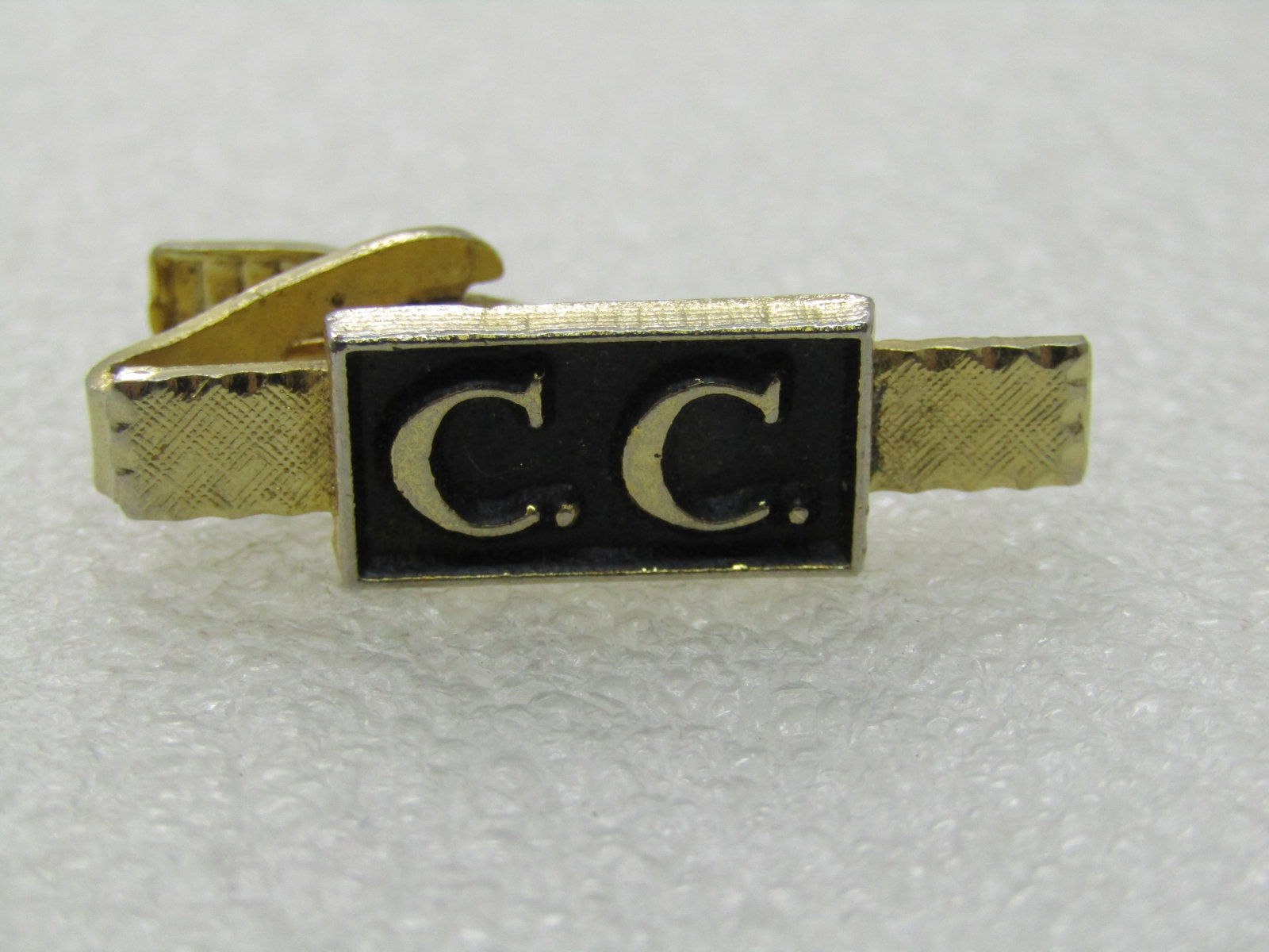Vintage C.C. Tie Clasp , 1.5", Gold Tone, 1960's: Vintage C.C. Tie Clasp , Gold Tone, 1960's. This is appx. 1.5" wide and slightly under 1/2" tall. Black enameled background framed in a .75" wide and nearly 1/2" tall rectangular set on top of the