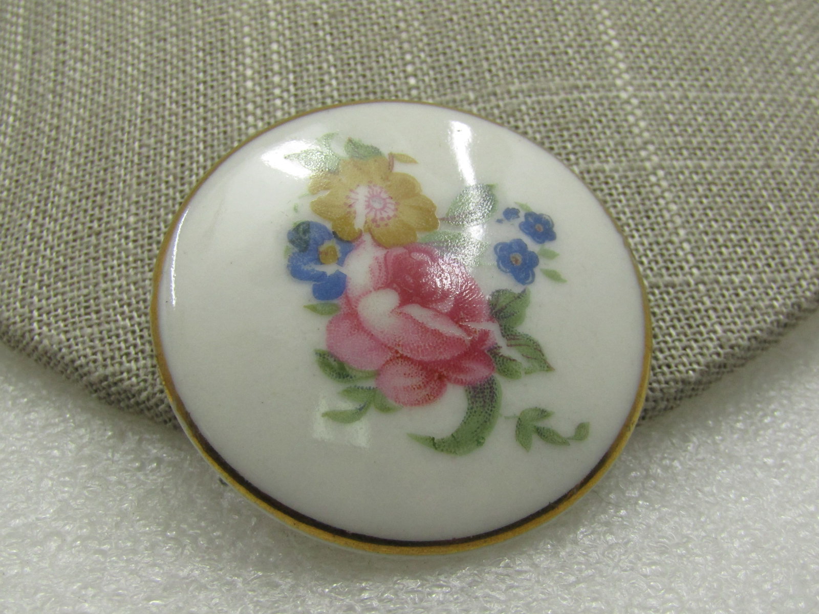 Vintage Porcelain Rose Gold Trimmed Brooch, 1.75" Round: Vintage Porcelain Rose Gold Trimmed Brooch, 1.75" Round. Yellow and Pink Rose with green leaves and blue cornflowers decal and trimmed with gold. The pinback has been reglued on the back. Age is