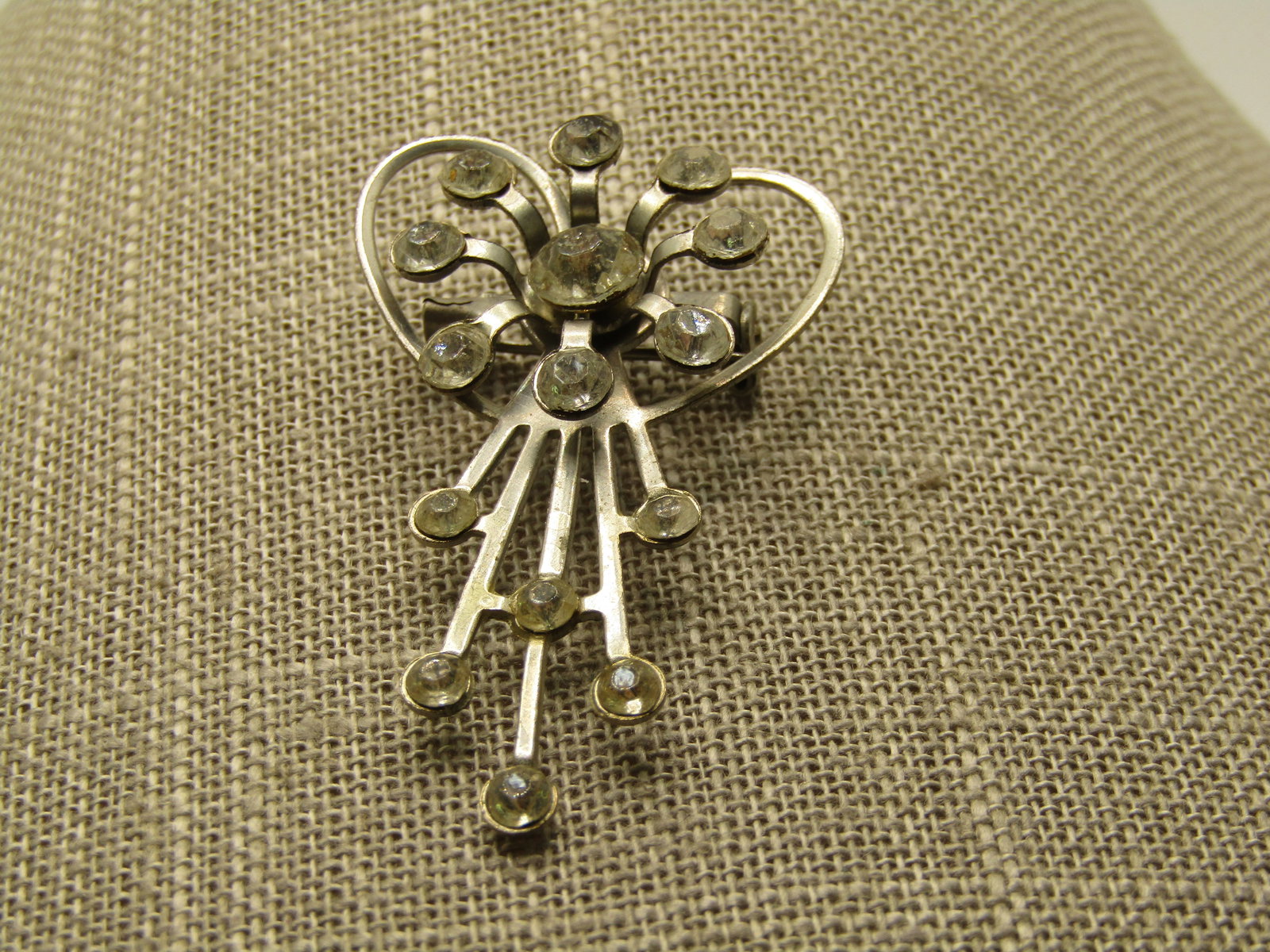 Vintage Rhinestone Heart/Ray Brooch, 1960's: Vintage Rhinestone Heart/Ray Brooch, 1960's, 2" long and 1.25" wide. Silver Tone. This has a background heart shape at tope with a rhinestone blossom over top and ray like drops with clear rhinestones