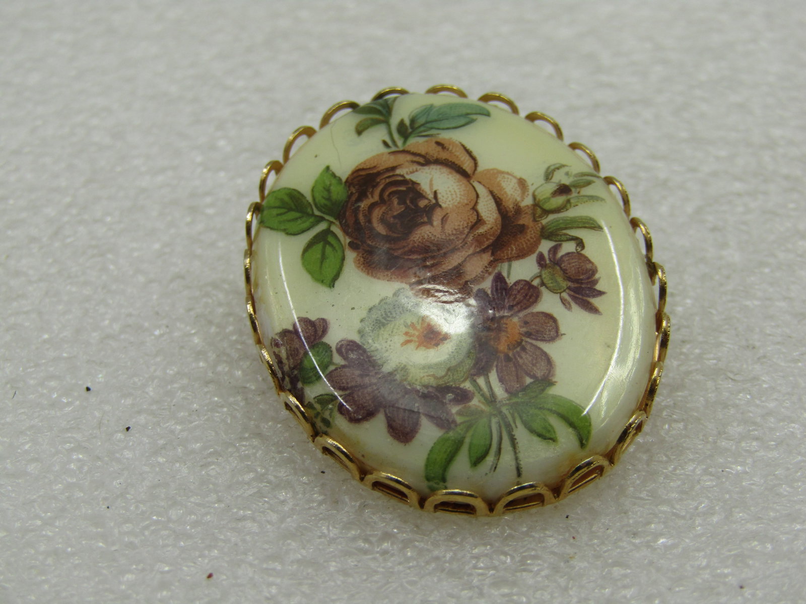 Vintage Floral Cameo Brooch, 1960'-1970's: Vintage Floral Cameo Brooch, 1960'-1970's, 1-5/8" by 1.25", gold tone open scalloped bezel with lavender to purple rose and other flowers with a white flower and green leaves. 1960's-1970's. Not