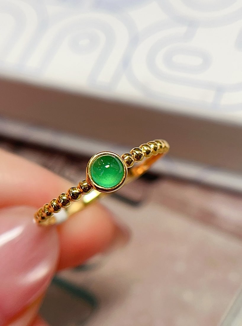 18K Gold Emerald Ring: Title: 18K Gold Emerald Ring Description: This ring features a natural emerald as the main stone, showcasing an enchanting round green hue. Its minimalist gold design perfectly accentuates the gem's r