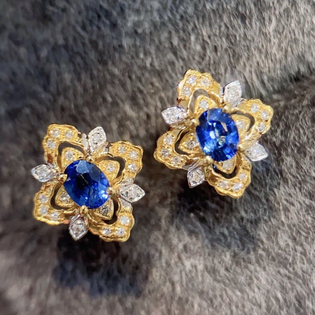 18K Gold Sapphire Earrings: Title: 18K Gold Sapphire Earrings Description: These earrings feature a deep royal blue sapphire as the visual centerpiece, adorned with brilliant small diamonds. The gold floral base outlines the