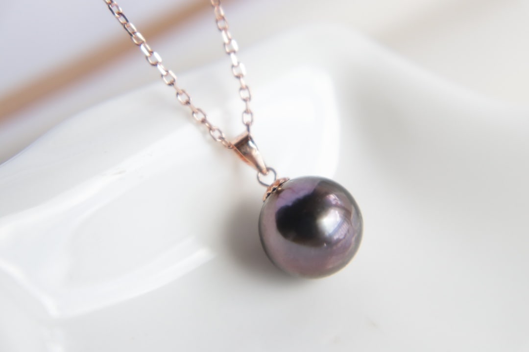 18K Gold Tahitian Pearl Pendant: Title: 18K Gold Tahitian Pearl Pendant Description: This 18K gold Tahitian pearl pendant is renowned for its perfect round shape and intense luster. The pearl exhibits an enchanting peacock green hue