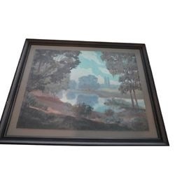 Framed Vintage Lakeside Landscape Print: This vintage print depicts a serene lakeside landscape, characterized by lush trees framing a body of water that reflects the sky and distant foliage. The art style evokes a sense of tranquil nature,