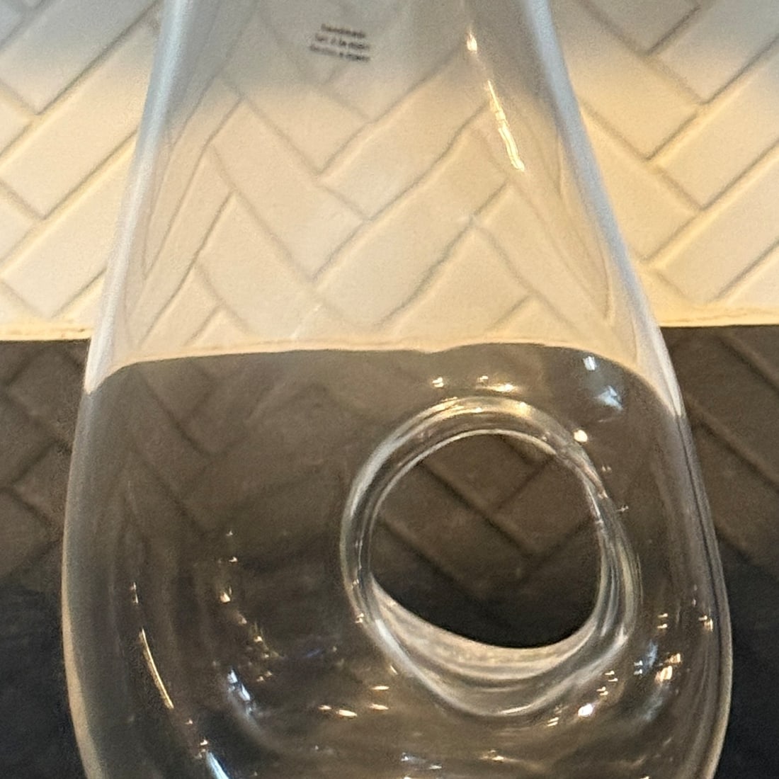 Ona Water Pitcher from Crate & Barrel: A contemporary clear glass carafe with a unique, integrated circular handle design, providing a sleek and seamless aesthetic. The piece features a gently flaring rim and a weighted base,