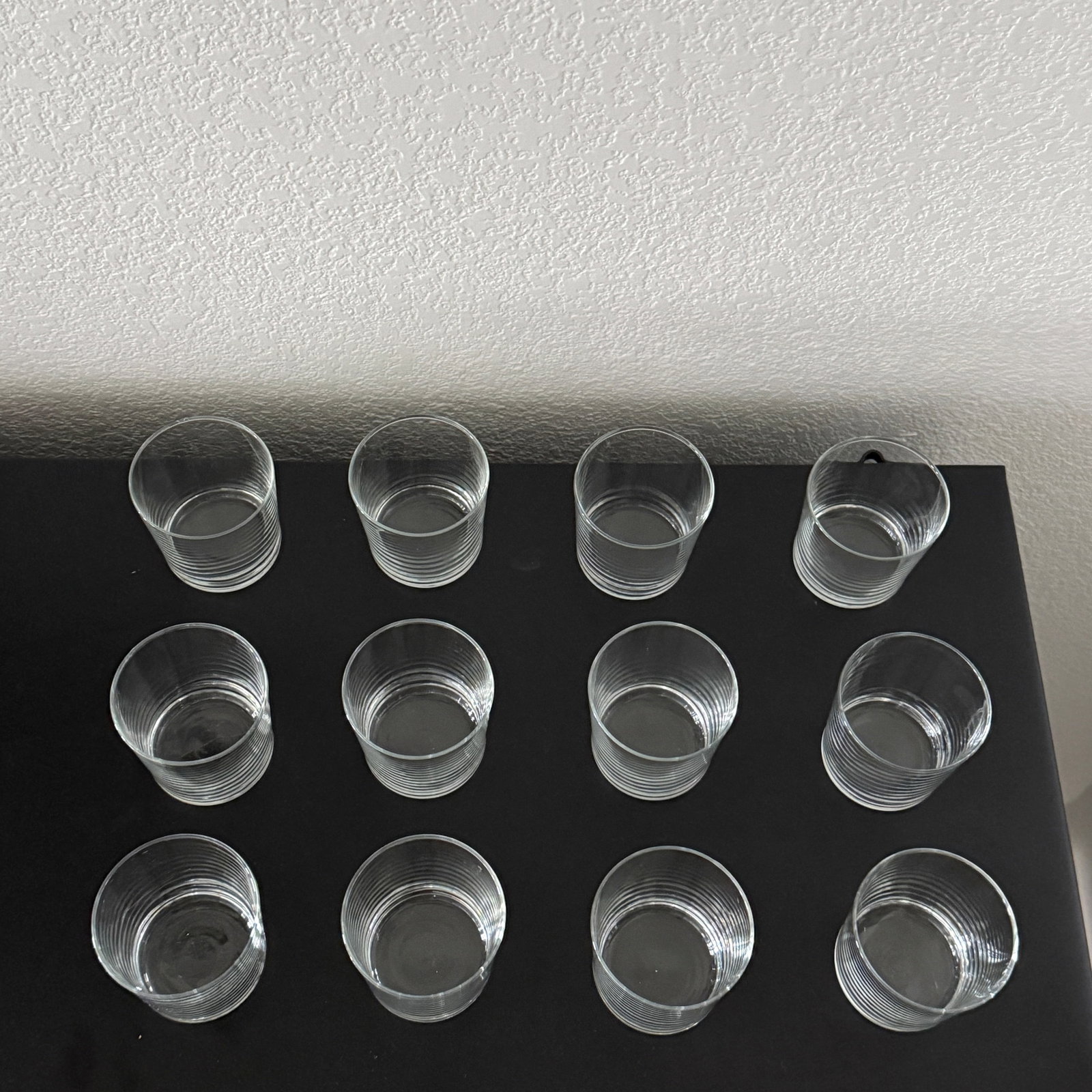 Set of Twelve Medium Clear Glass Tumblers: This lot features a set of twelve clear glass tumblers, each adorned with a subtle paneled design around the body. The tumblers have a sturdy, thick base and a smooth rim, suggesting a blend of durabi