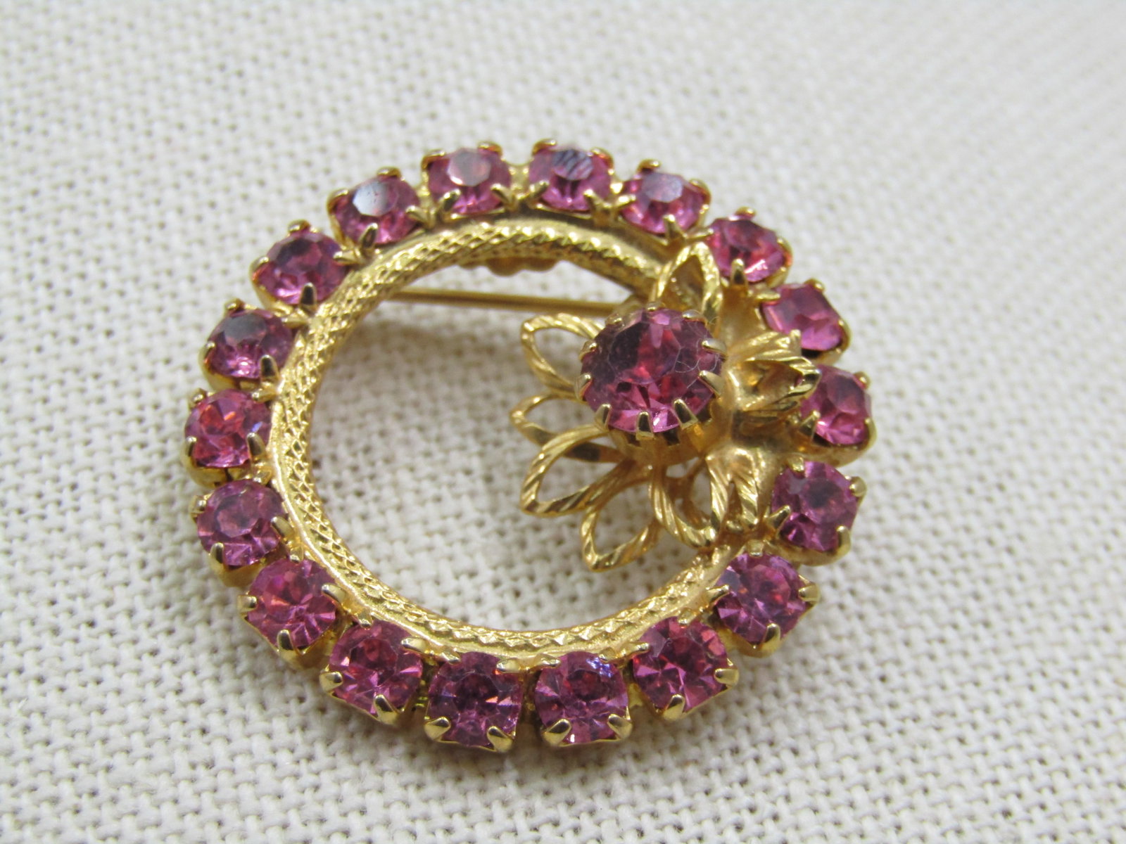 Vintage Pink Rhnestone Circle Brooch, 1970's, 1.25": Vintage Pink Rhnestone Circle Brooch, 1970's, 1.25". Blossom like accent top center. Gold tone. Very good condition. Not signed by the maker. (INV. W830-101114.6 SS6348 J LD 1/5/22). Reserve: $25.00