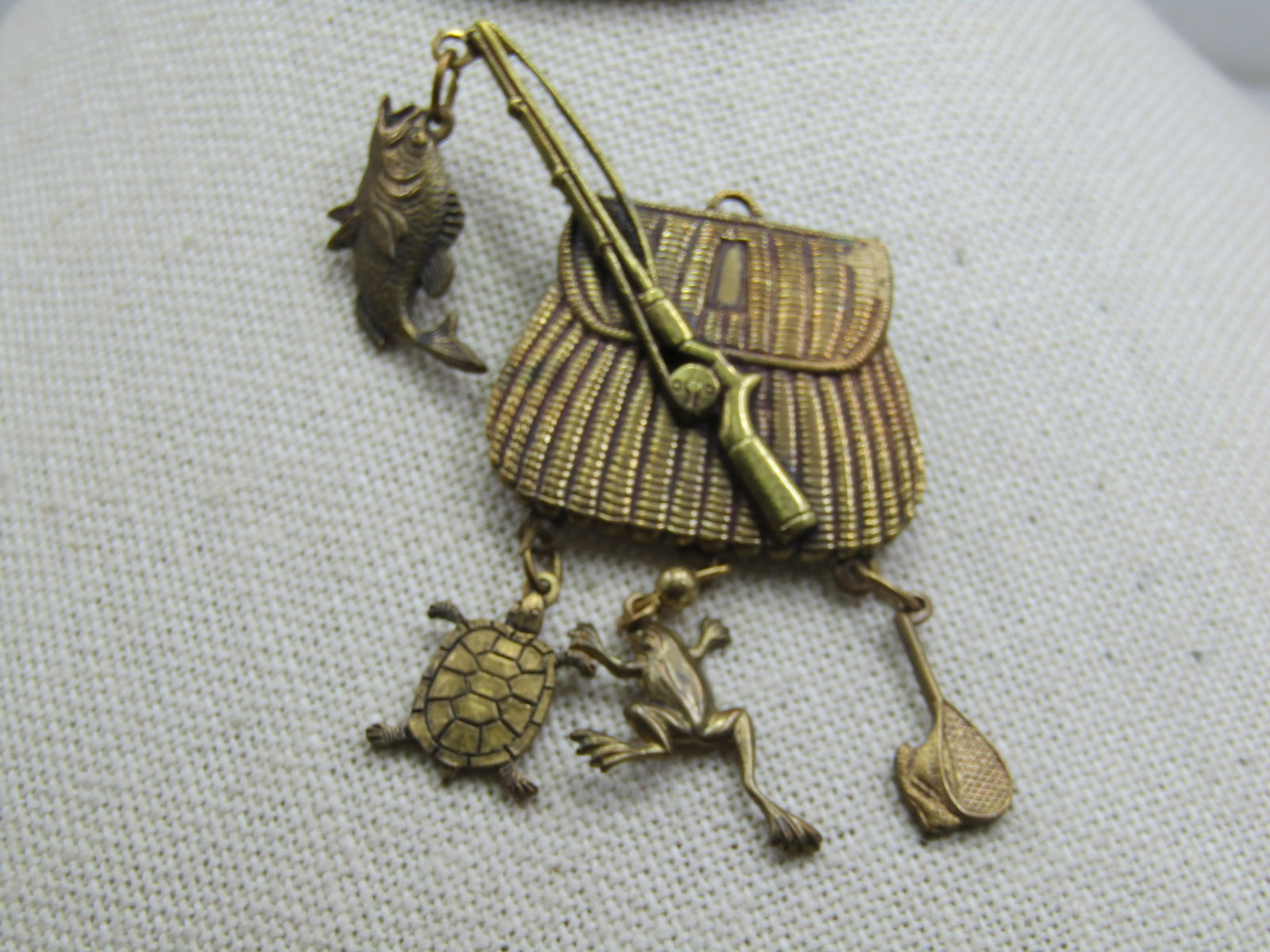 Vintage Fishing Creel, Rod and Dangles Brooch, 2.25" by 1.75": Vintage Fishing Creel, Rod and Dangles Brooch, 2.25" by 1.75". Brass tone pressed metal done very nicely with a woven textured creel and a rod overlaid over that with a fish dangling from the tip fo t