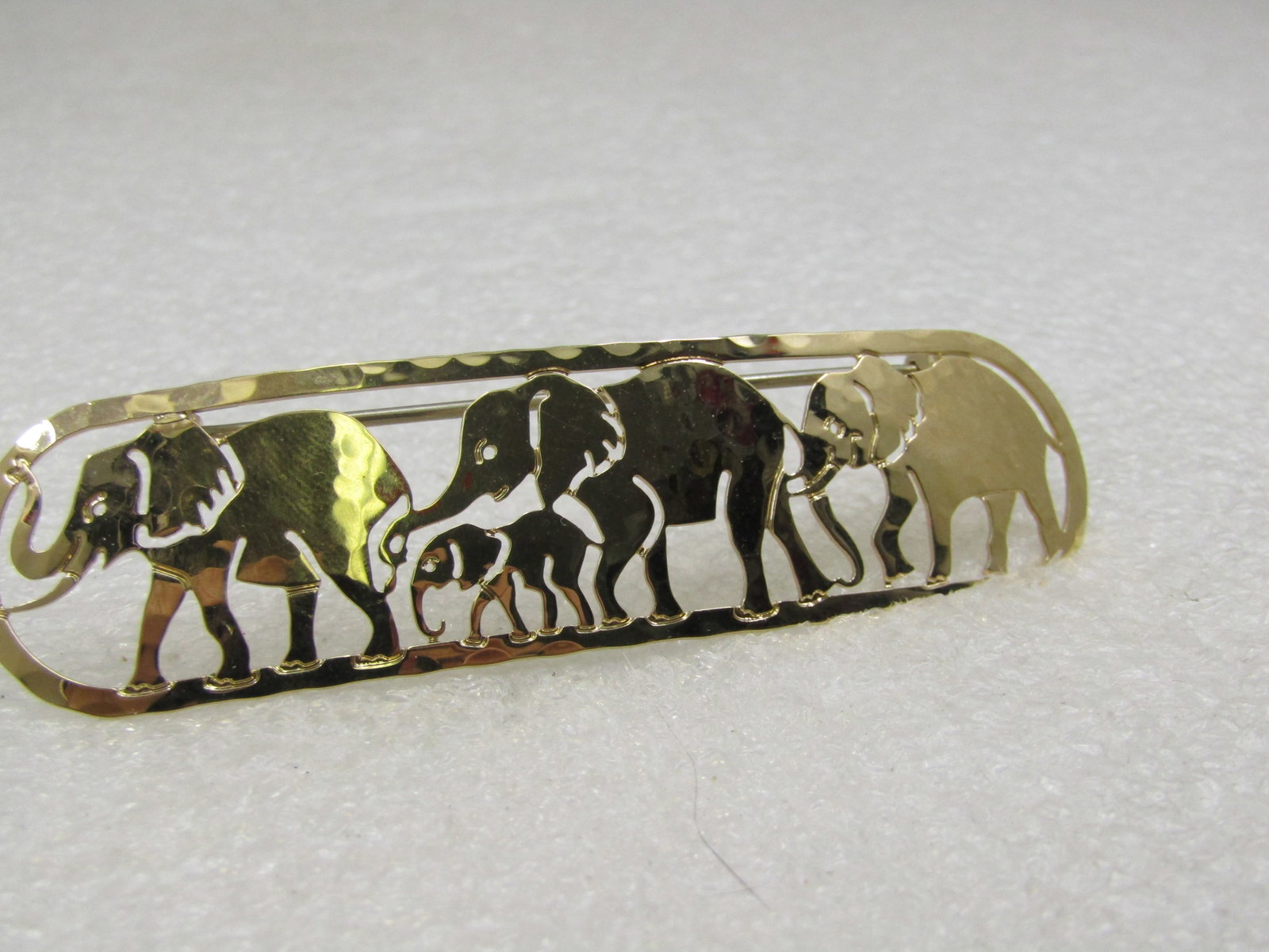 Vintage Elephant Brooch Signed Wild Bryde, Cut-Out, 3" by 3/4": Vintage Elephant Brooch Signed Wild Bryde, Cut-Out, 3" by 3/4" gold tone hammered cutout metal design with three adult elephants walking in a ine with a baby between the first two. Elongaged oval.