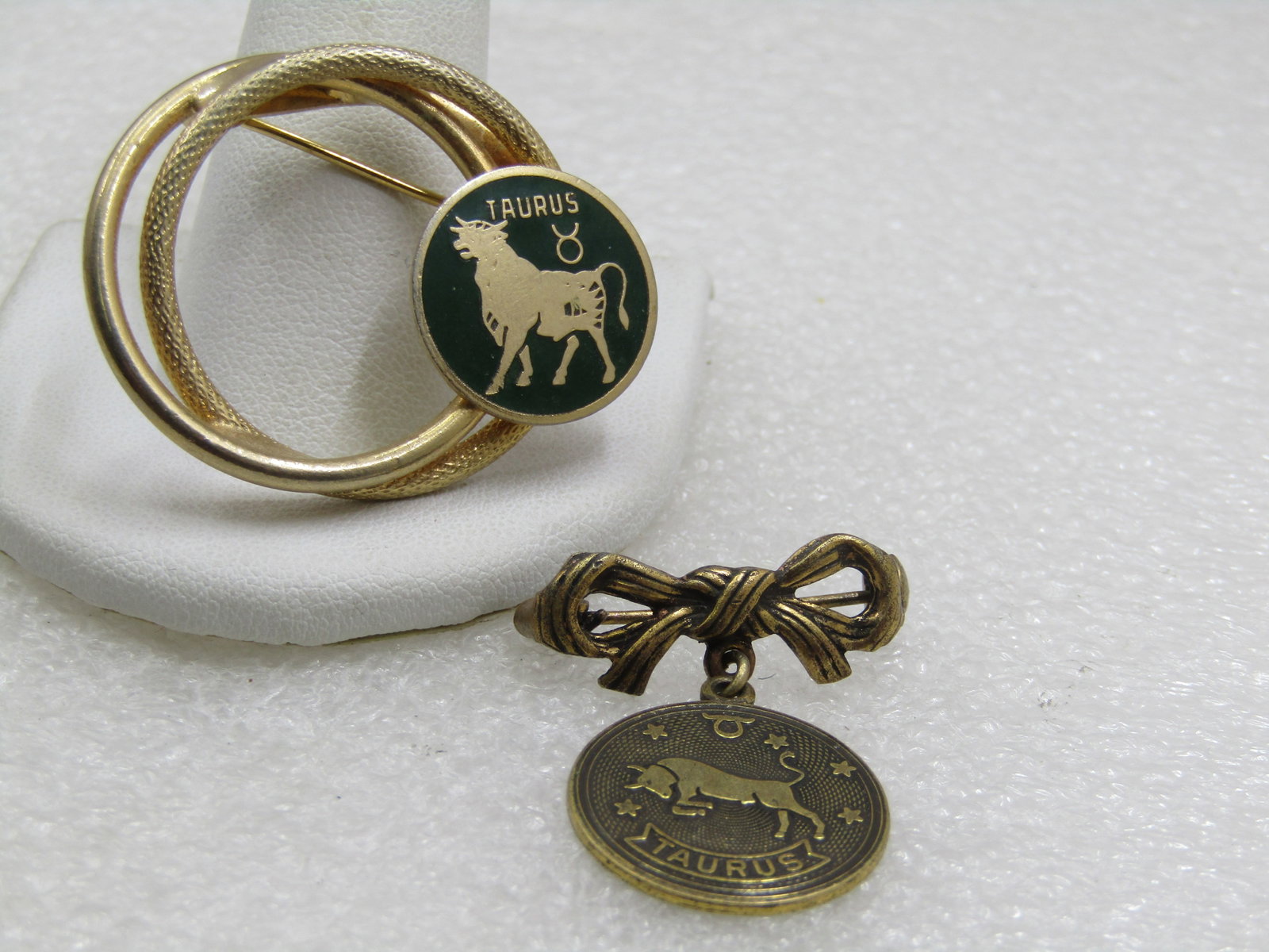 Vintage Pair Taurus Zodiac Brooches, 1960's-1970's: Vintage Pair Taurus Zodiac Brooches, 1960's-1970's. One is a double circle, one smoth and one textured brooch with a green enameled Taurus symbol set on the right side. The brooch is 1.25" tall and 1.