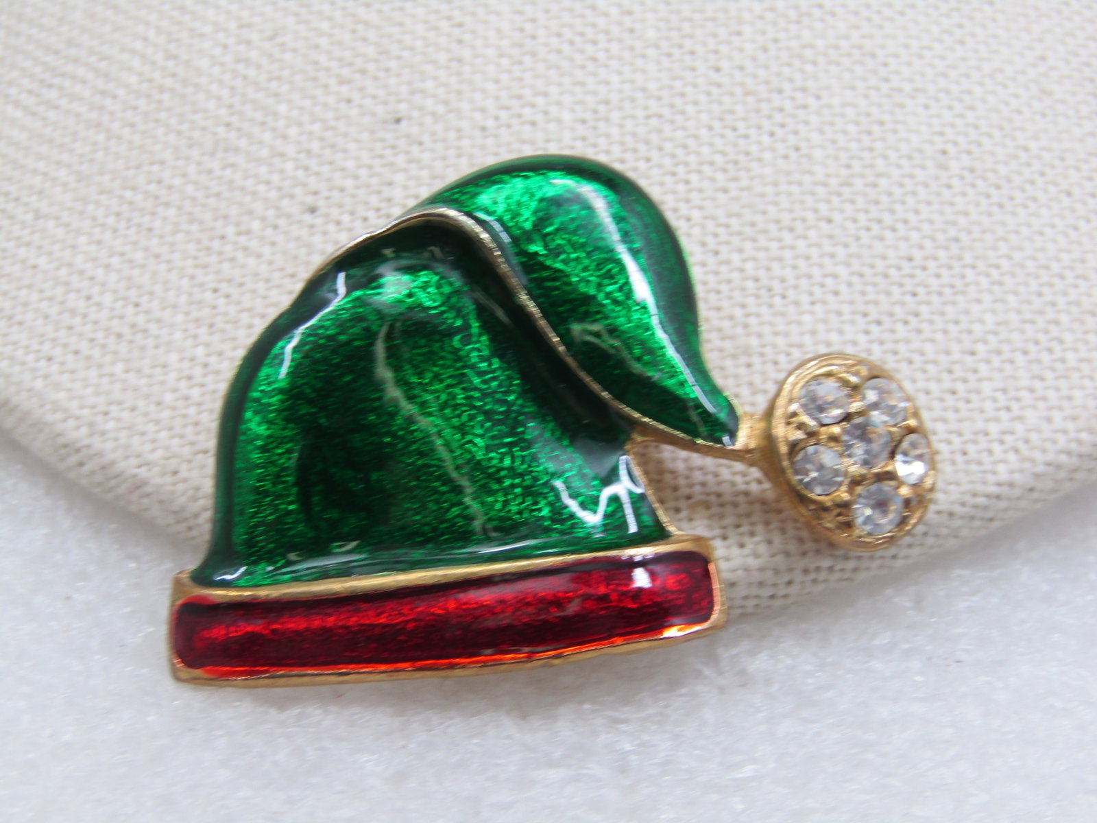 Vintage Clioisonne Red & Green Santa Cap with Rhinestones: Vintage Clioisonne Red & Green Santa Cap with Rhinestones. 1.5" tall and 2" wide. Six clear rhinestones in the puff at the end of the cap. Gold tone metal. Age is appx. 1970's. Very good condition.