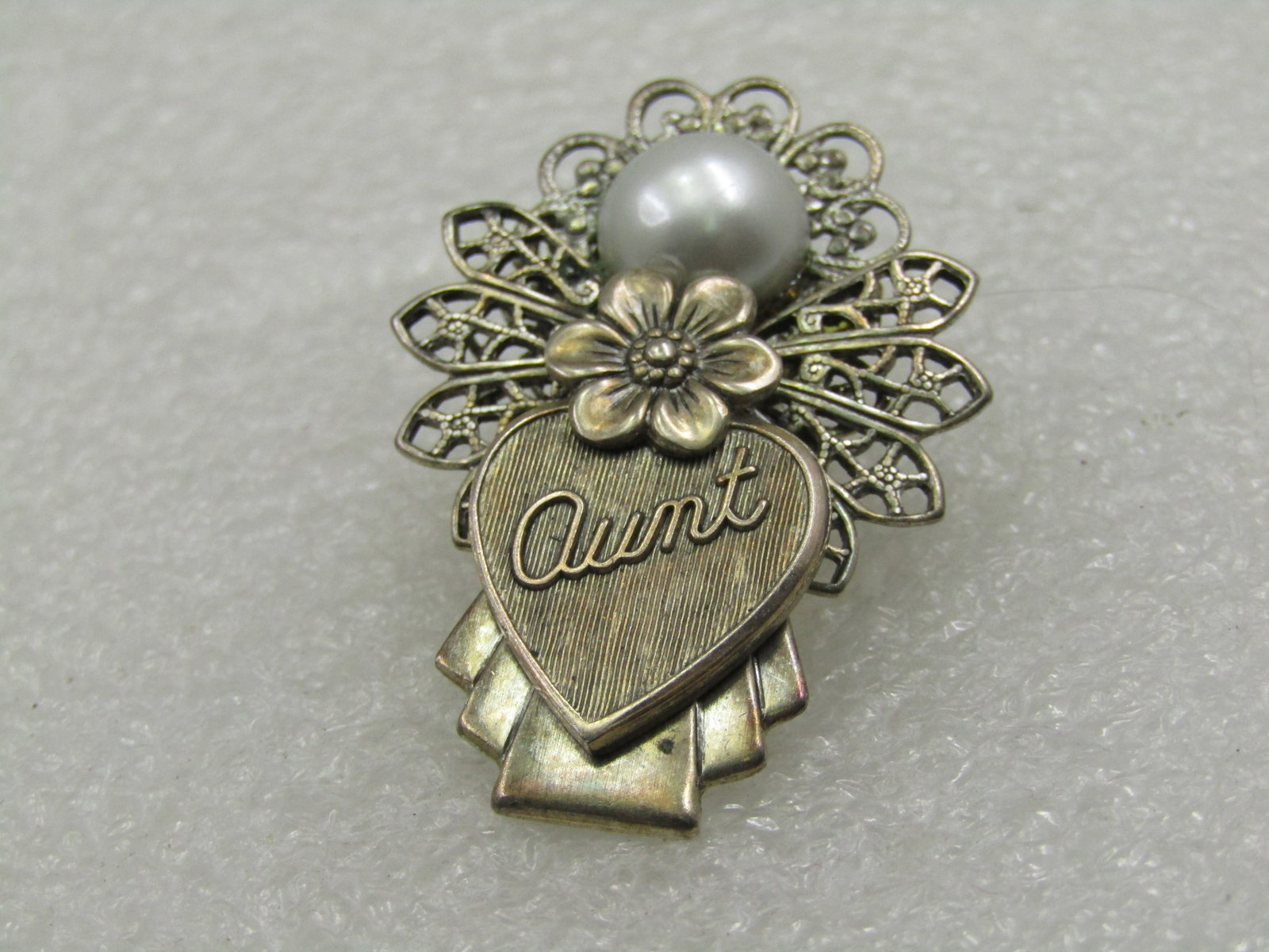 Vintage Filigree Aunt Angel Brooch, Silver Tone, 1.5": Vintage Filigree Aunt Angel Brooch, Silver Tone, 1.5" tall and appx. 1-1/8" wide. Silver tone with an 8mm half round faux pearl face, floral accent and a charm in front that has cursive Aunt on the