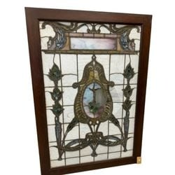 An American Leaded and Stained Glass Window Panel, circa 1900: This rectangular leaded and stained glass window panel, dating to approximately 1900, features a central medallion with scrolling foliate and stylized urn designs. The medallion is flanked by