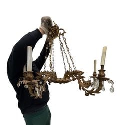 Gilt Metal and Crystal Chandelier: This ornate chandelier is crafted from gilt metal, featuring an openwork foliate design with scrolling leaves and floral accents. It is embellished with numerous faceted crystal pendants and beads,