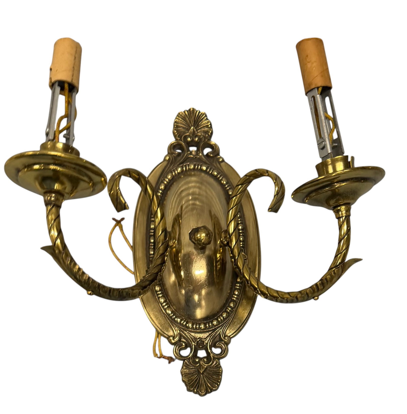 Pair of Rococo Revival Gilt Brass Sconces: A pair of Rococo Revival gilt brass two-light wall sconces, likely early 20th century. Each sconce features an ornate oval backplate with a central shell motif and scrolling acanthus leaf details, fla