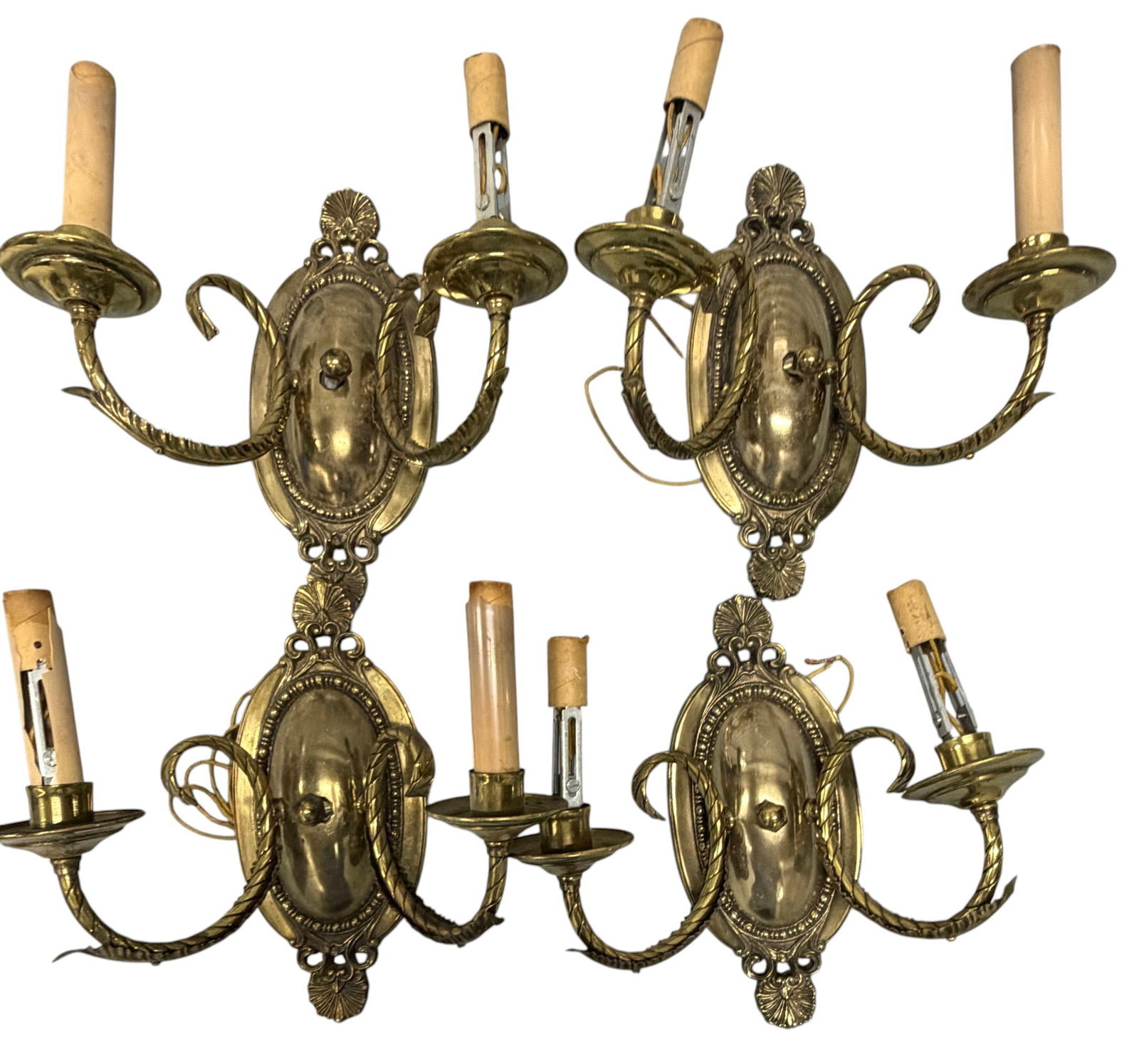 Set of Four Brass Wall Sconces, Neoclassical Style: A set of four ornate brass wall sconces, featuring a neoclassical design. Each sconce has a central oval backplate adorned with foliate and shell motifs, from which two scrolling arms extend to hold