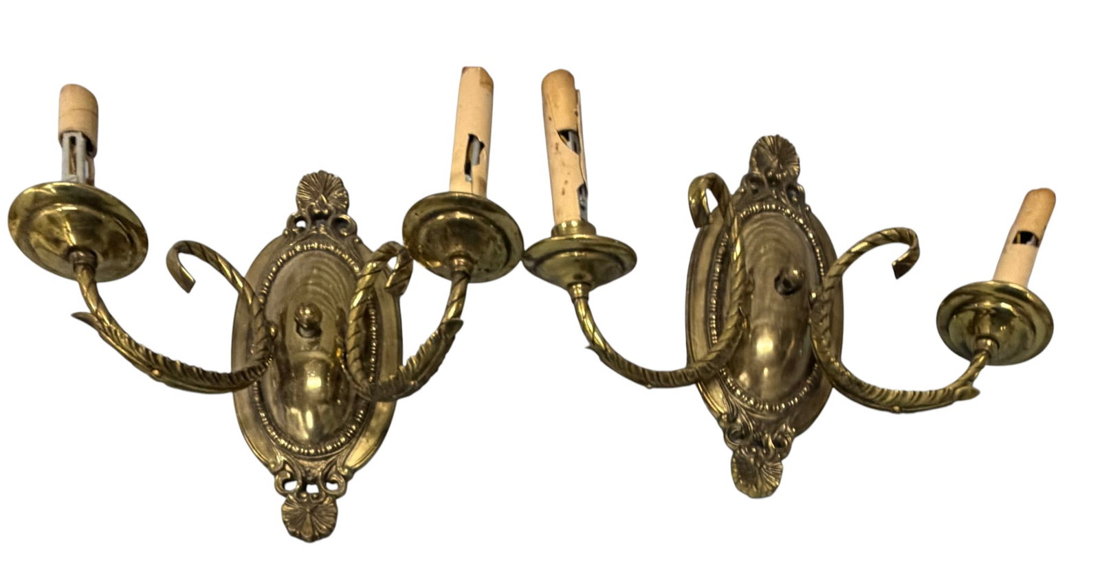 Pair of Rococo Revival Brass Sconces: A pair of Rococo Revival brass sconces, likely dating from the mid-20th century. Each sconce features an ornate oval backplate with rocaille and foliate motifs, supporting two S-curved arms. The arms