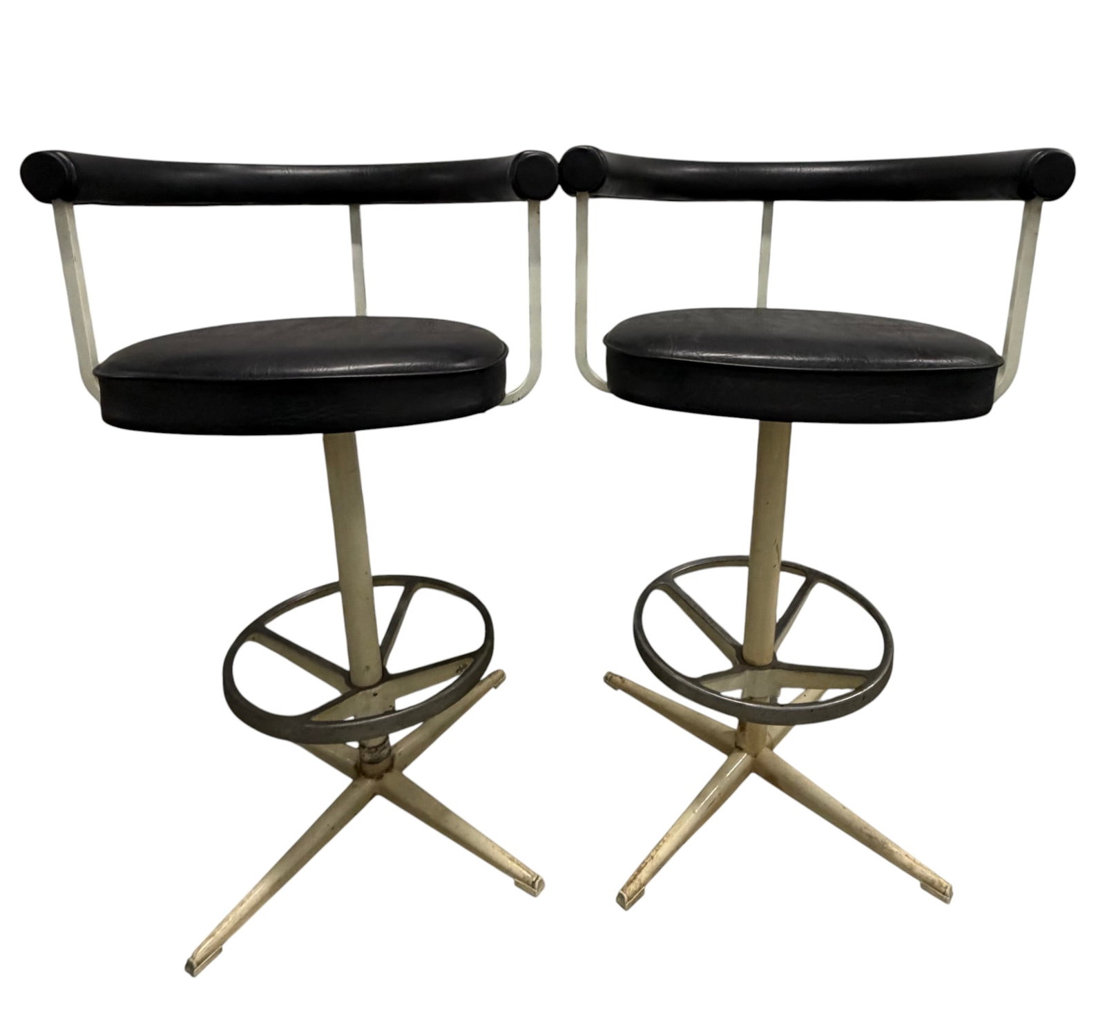 Pair of Mid-Century Modern Swivel Bar Stools: A pair of Mid-Century Modern swivel bar stools, circa 1950s-1960s. These stools feature black vinyl upholstered circular seats and curved backrests, supported by white enameled metal frames. The