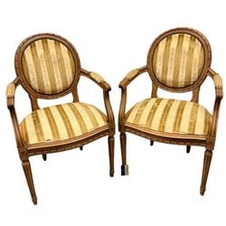 Pair of Louis XVI Style Carved Wood and Upholstered Armchairs: A pair of Louis XVI style armchairs, likely early-to-mid 20th century. Each chair features a carved wooden frame with classic Neoclassical motifs, including fluted legs and carved rosettes. The oval b