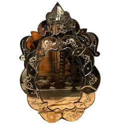 Venetian Style Etched Glass Wall Mirror: This ornate wall mirror is crafted in the Venetian style, featuring an elaborately shaped wooden frame adorned with numerous individual pieces of etched and beveled mirror glass. The glass panels are