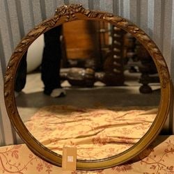 Giltwood Oval Wall Mirror with Fretwork Crown: An elegant giltwood oval wall mirror from the mid-20th century, presented in the Rococo Revival style. The mirror features a carved wood frame with a distressed gilt finish, adorned with classical