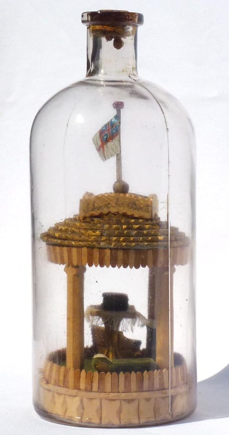 A very intricate carved and tramp art bottle whimsy.: This is a very intricate bottle whimsy. It contains a pavilion with carved pillars and a tramp art roof. Inside the pavilion are a table covered with a fringed cloth with a large Bible on top, a sofa
