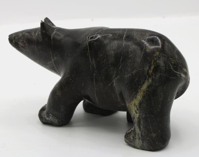 An Inuit carved folk art stone black polar bear from Alaska.: This polar bear of Alaskan folk art is carved from black stone with lighter veins. Its facial features are carved in detail. It is in very good condition with a chip on the tip of one ear. The size