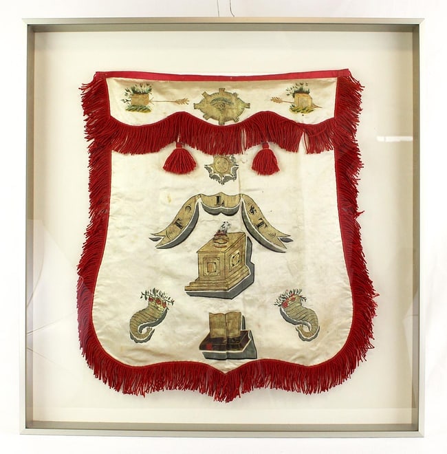 An Oddfellows ceremonial apron professionally mounted: This is an Oddfellows ceremonial apron. It is fringed silk, painted with fraternal symbols including the All-Seeing eye, sun, and Bible. It has been professionally mounted in a frame 26" high by 25