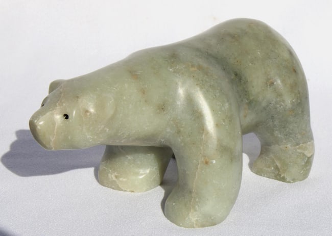 An Inuit carved folk art stone white polar bear from Alaska.: This is a carved stone polar bear from a collection of Alaskan folk art. It is carved from white and gray stone, with painted eyes. It measures 7" long by 3 1/2" high by about 3 1/2" wide, in