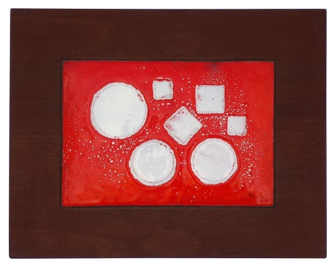 A colorful Mid-Century modern style enameled plaque: This is a colorful Mid-Century modern style enameled plaque set in a frame cut from a single piece of wood. It has geometric squares and circles of white on a red background highlighted with
