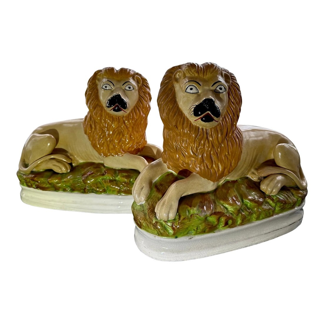 Pair of 19th Century Staffordshire Lions From England: Pair of stylish English Staffordshire lions. Lovely large scale which is unusual and rare. The figures are whimsical lying lions on beds of green grass, with their tails curling back around their