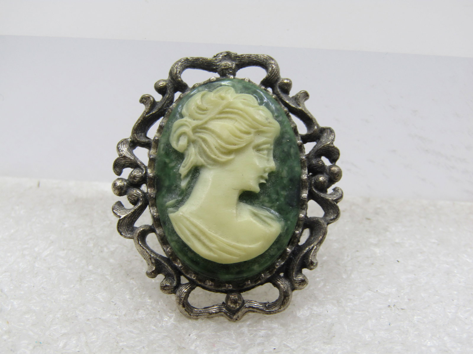 Vintage Green & White Cameo Brooch, 1940's-1950's: Vintage Green & White Cameo Brooch, 1940's-1950's. This has a silver tone filigree scrolled frame around a green and white molded cameo. It is appx. 1.5" tall and 1" wide with a bezel-setting to the c