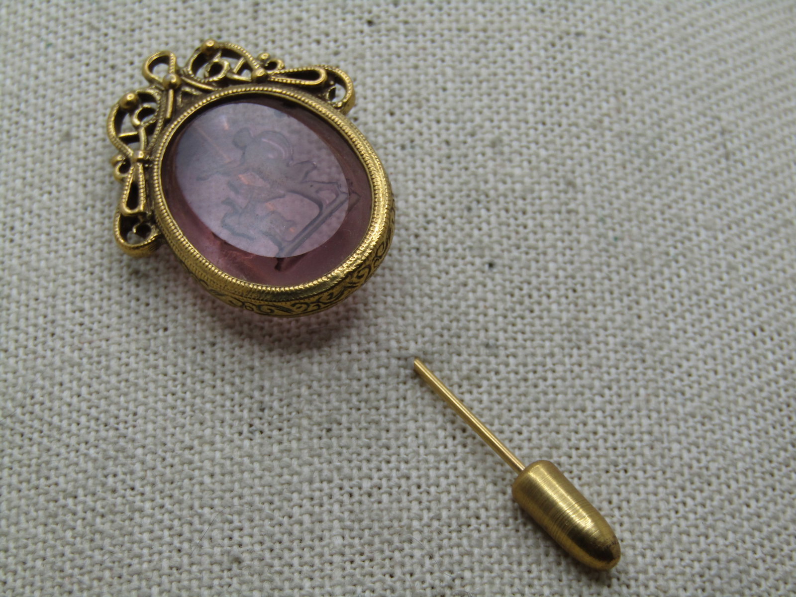 Vintage Purple Glass Angel Cameo Stick Pin, Reverse Carved, 1960's-1970's: Vintage Purple Glass Angel Cameo Stick Pin, Reverse Carved, 1960's-1970's. Gold tone with a scrolled elaborate top to the oval reverse cut purple glass angel cameo . The glass is appx. 1" by 3/4" set 