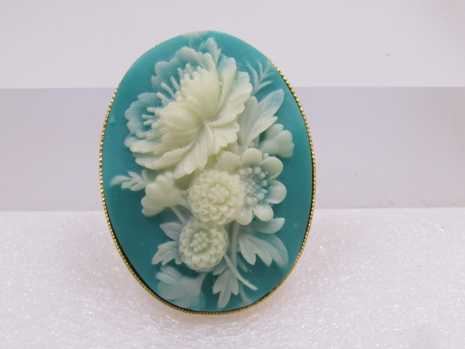 Vintage Aqua & White Floral Cameo Brooch, 1960's-1970's: Vintage Aqua & White Floral Cameo Brooch, 1960's-1970's. Gold tone and appx. 1.75" by 1.25" with the cameo style brooch having a acrylic aqua base and raised molded white floral design on top. Ridged 