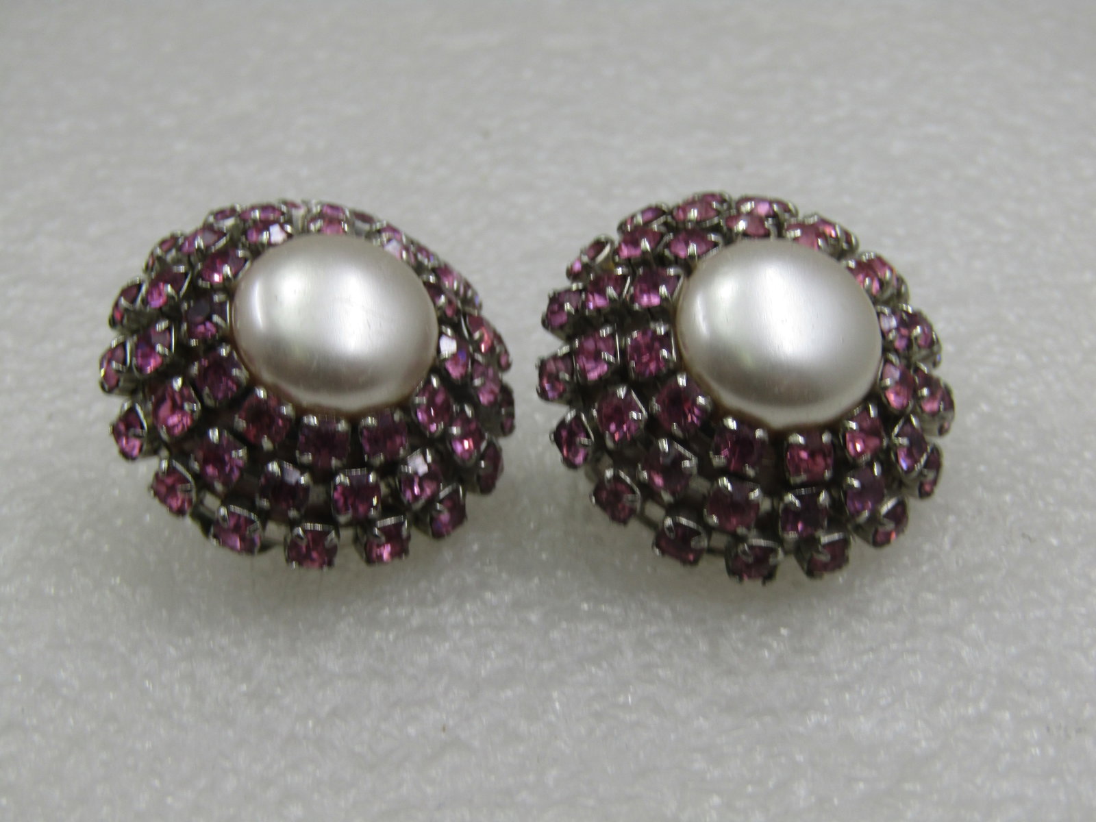 Vintage Faux Pearl Pink Rhinestone Clip earrings, Mid-Century: Vintage Faux Pearl Pink Rhinestone Clip earrings, Mid-Century. 1-1/8" round with three rows of pink 2.5mm round rhinestiones tapered from wider at the bottom to where those stones are a halo around an