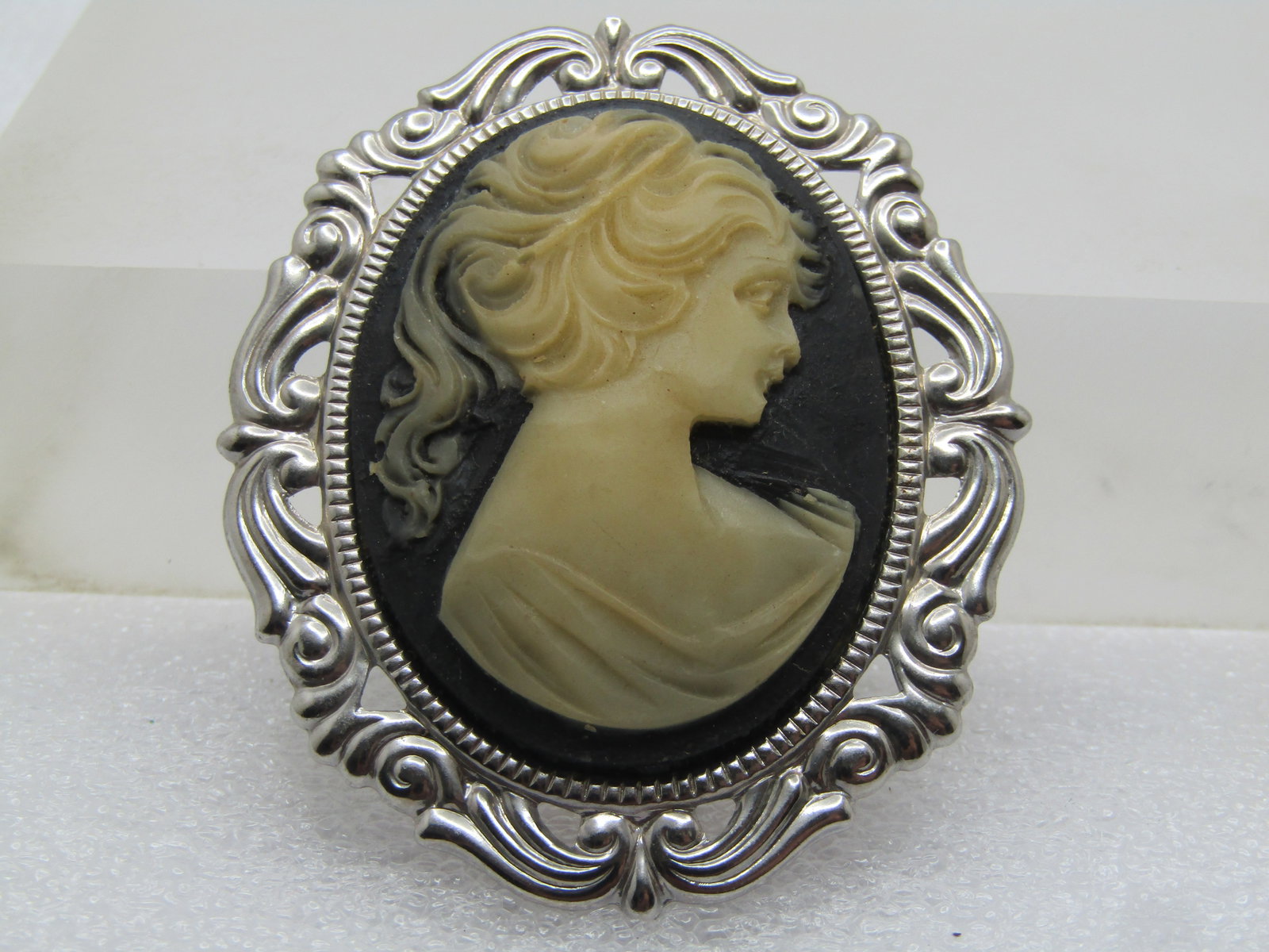Vintage Cameo Brooch, 1950's-1960's, Black & White: Vintage Cameo Brooch, 1950's-1960's, Black & White. Silver tone fancy frame and closed back with locking clasp. it is appx. 2.25" tall and slightly over 1.75" wide. It is not signed or marked. Very go