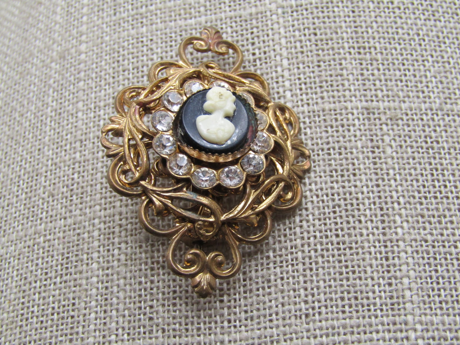 Vintage Cameo Rhinestone Filigree Brooch, 1940's-1950's: Vintage Cameo Rhinestone Filigree Brooch, 1940's-1950's. Gold tone with locking clasp. Scrolled design with heart scrolls off to each side. Black and white molded cameo set on top with a sawtooth ezel