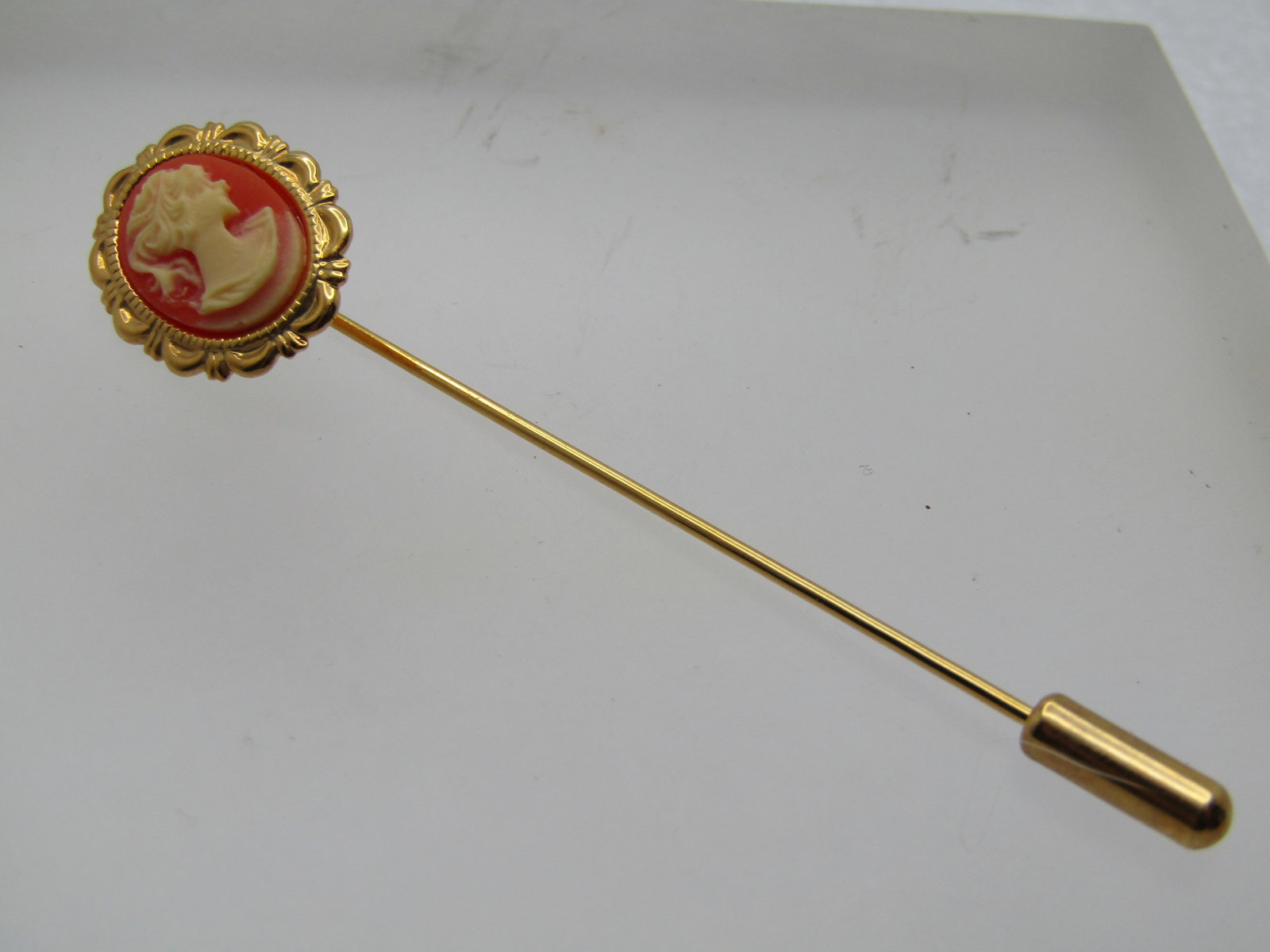 Vintage Cameo Stick Pin, 1960's-1970's, Gold Tone: Vintage Cameo Stick Pin, 1960's-1970's, Gold Tone with safety cap. It is appx. 3" long and the cameo is appx. 3/4" by 5/8" oval with a pressed or molded cameo in an orange-ish background and white fac