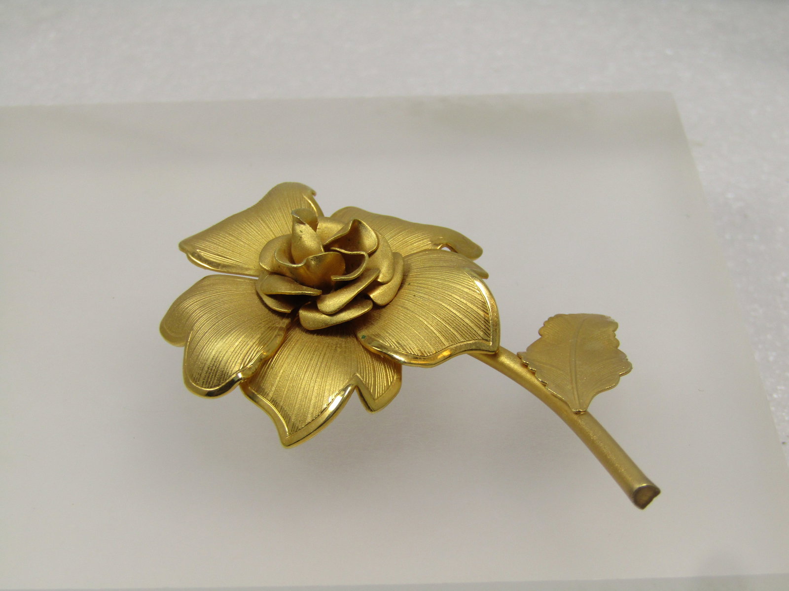 Vintage Rose Stem Brooch, Gold Tone, 1960's-1970's: Vintage Rose Stem Brooch, Gold Tone, 1960's-1970'stextured leave and blossom with smooth curved stem. The brooch is appx. 2.5" tall and 1.5" wide. The center of the rose is raised like an opening but
